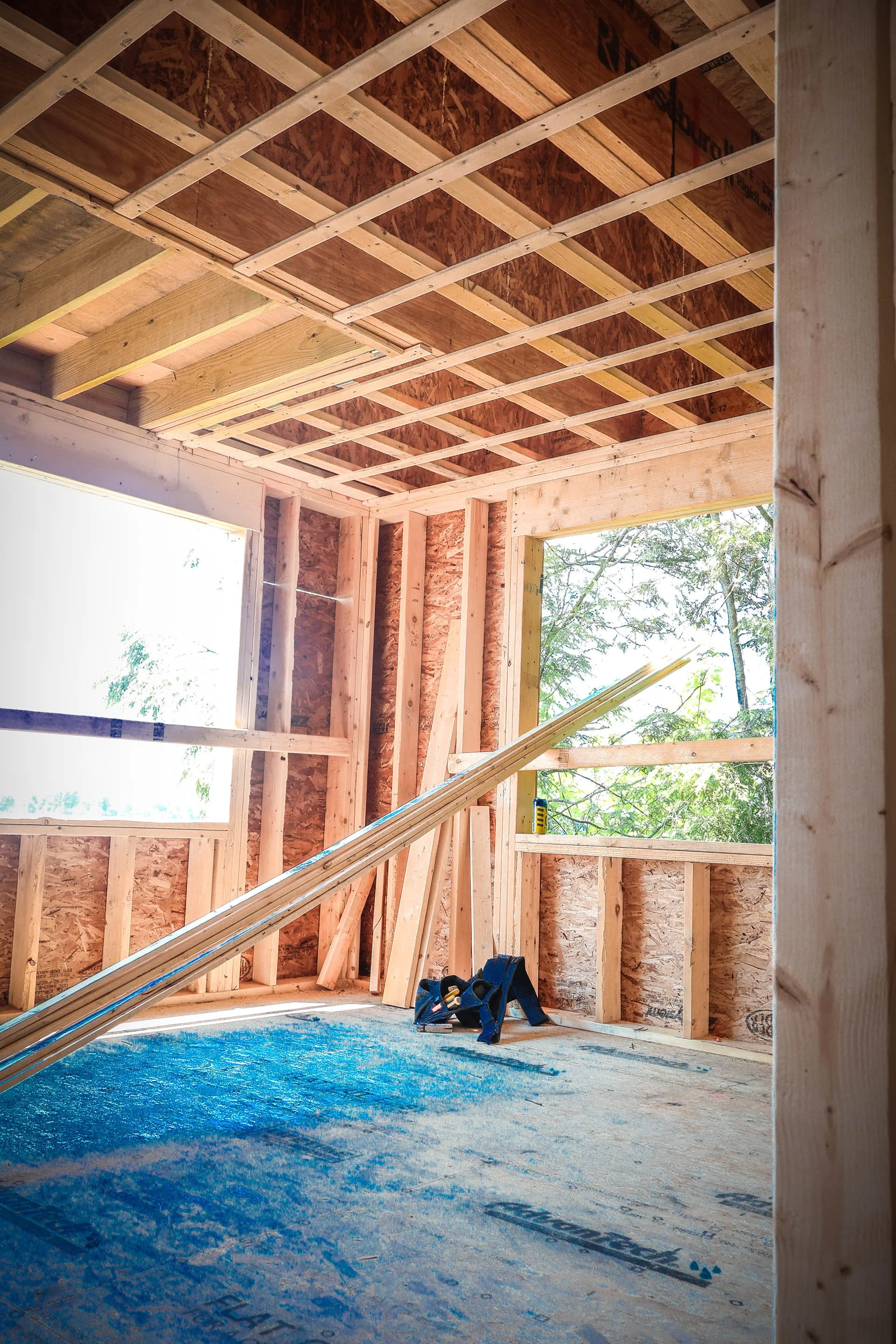 Interior view of a house under construction with wooden framing, open window, and construction tools on the floor.