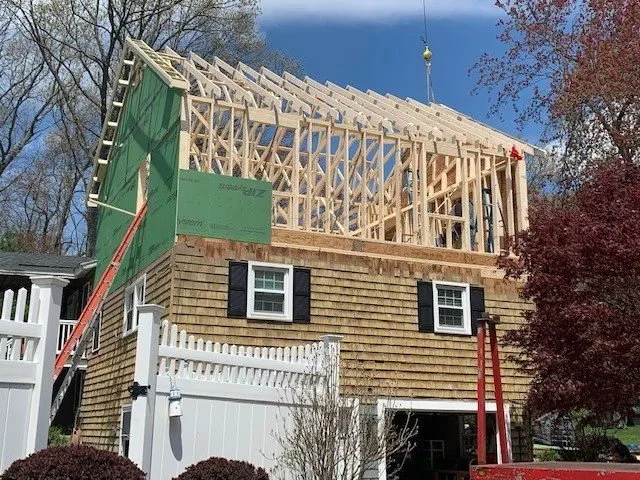House under construction with wooden framework on the upper floor, scaffolding, and a crane in the background.