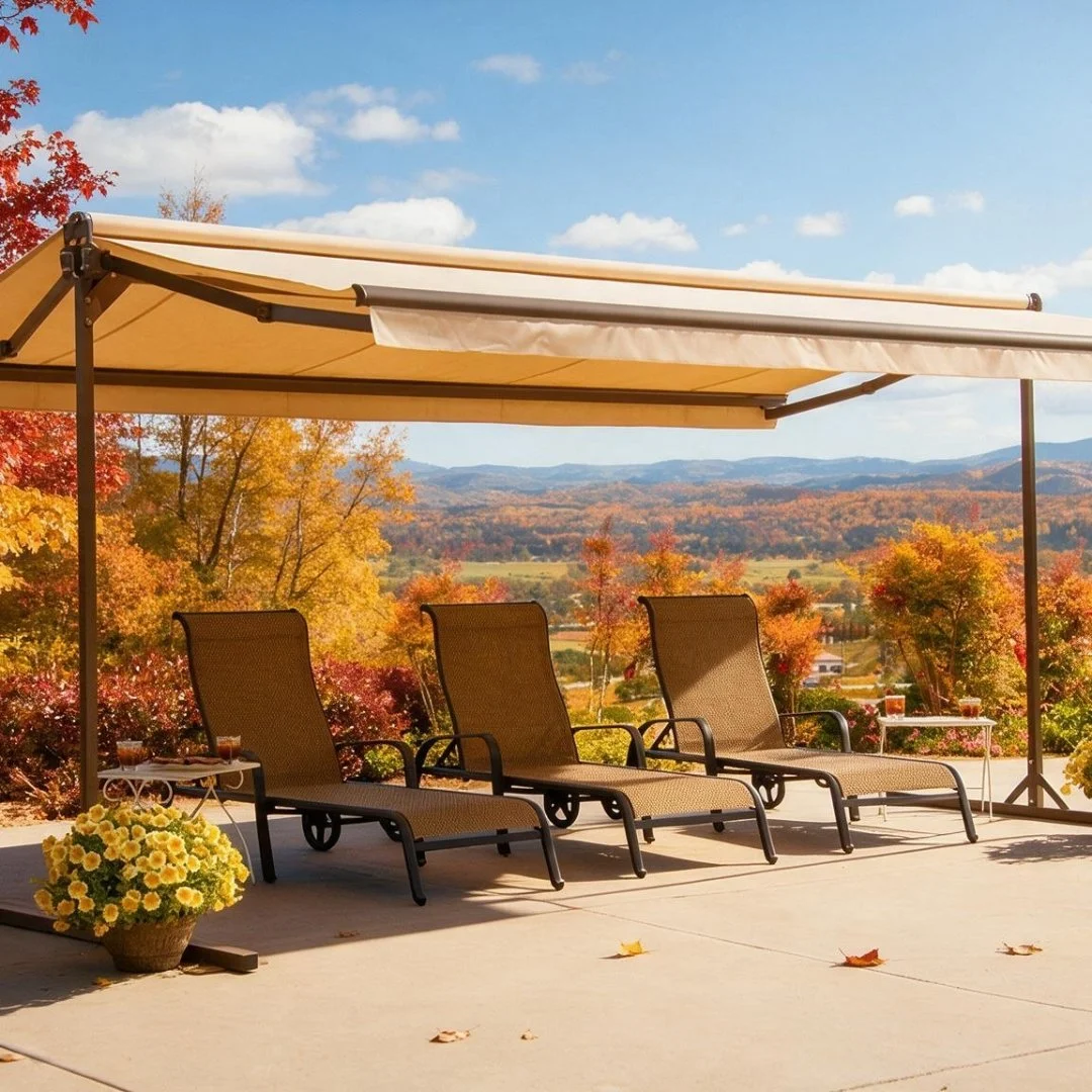 Three lounge chairs under a beige patio canopy on a concrete patio, with fall-colored trees and mountains visible in the background.