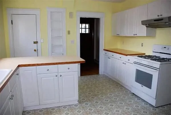 A kitchen with white cabinets, wooden countertops, a stove, and yellow walls.