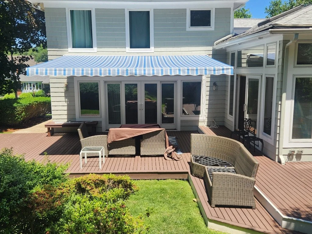 Backyard patio with outdoor furniture, a striped blue and white awning, and a house with multiple glass doors and windows.