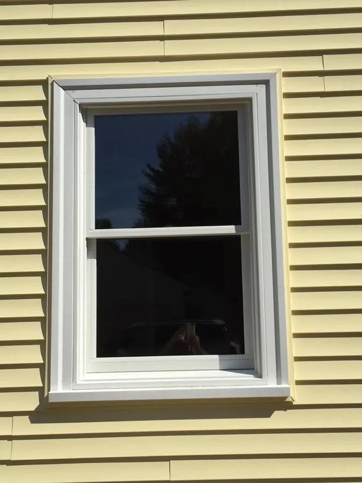 A yellow house exterior featuring a white-framed double-hung window with open shutters, reflecting trees and the dark sky.