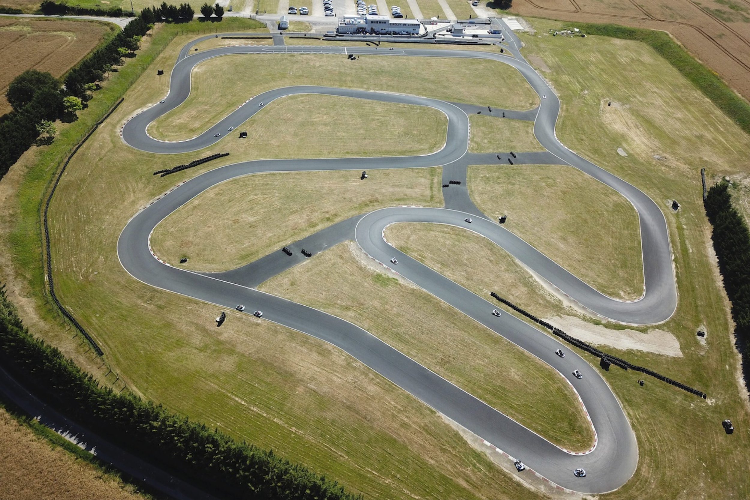 Une piste de course pour voitures, avec plusieurs virages serrés et courbes, vue aérienne sur un terrain vert entouré de champs.