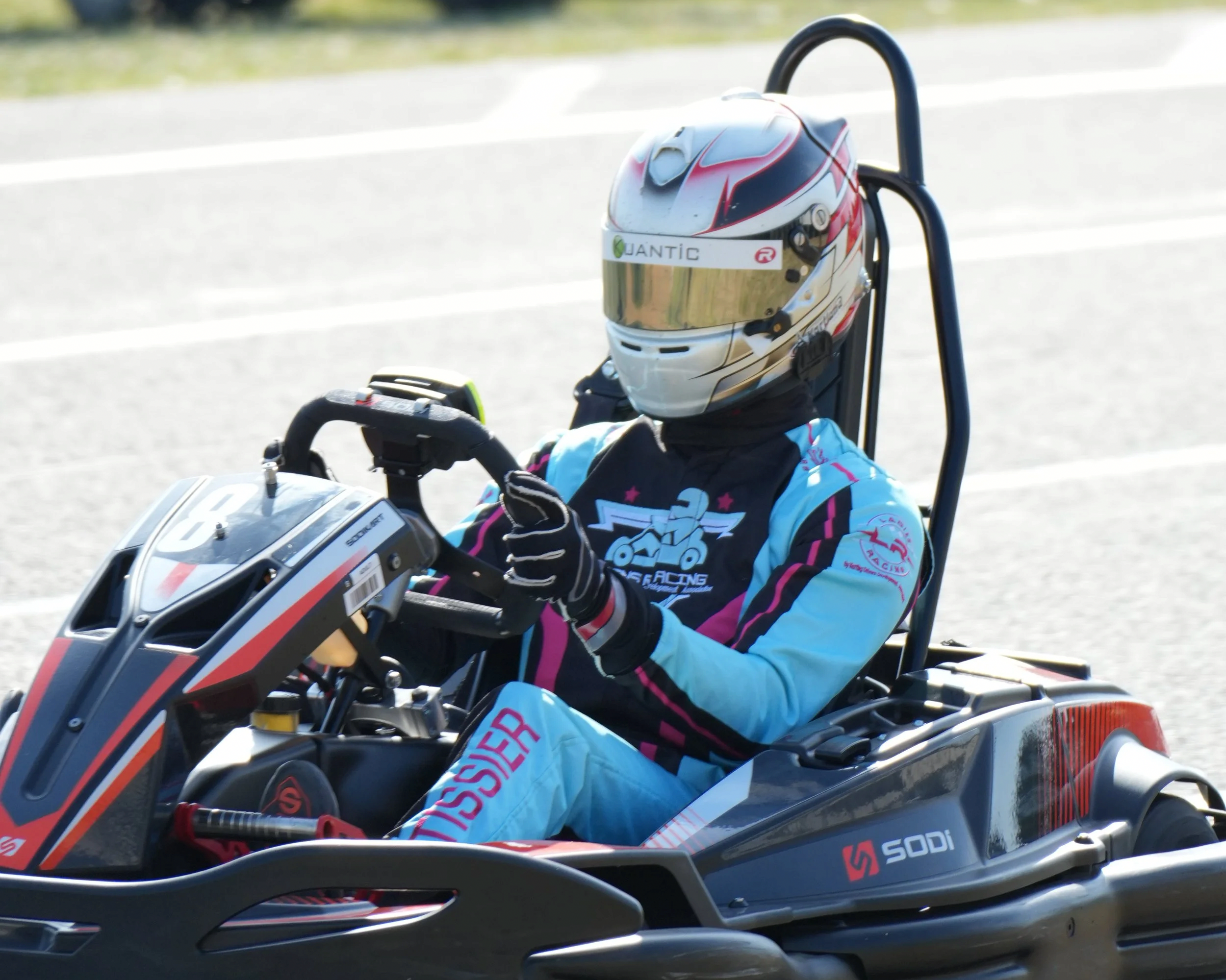 Un pilote portant un casque blanc et une combinaison de course bleue assis dans une voiture de course Gokart