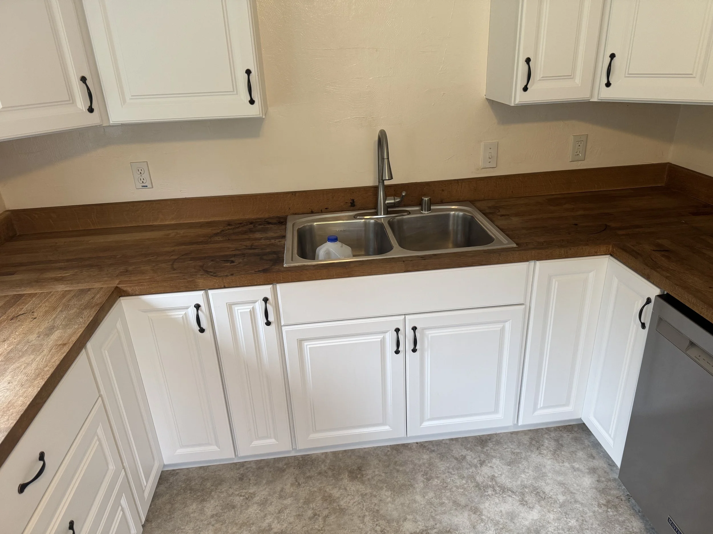Kitchen sink with a wooden countertop, white cabinets, and a small milk jug inside the sink.