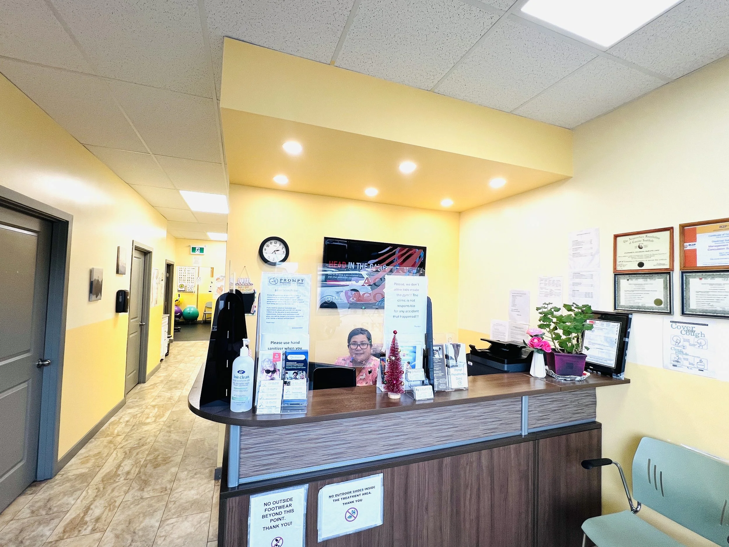 Hospital reception desk with a computer, potted plants, colorful decorations, and framed certificates on the wall.