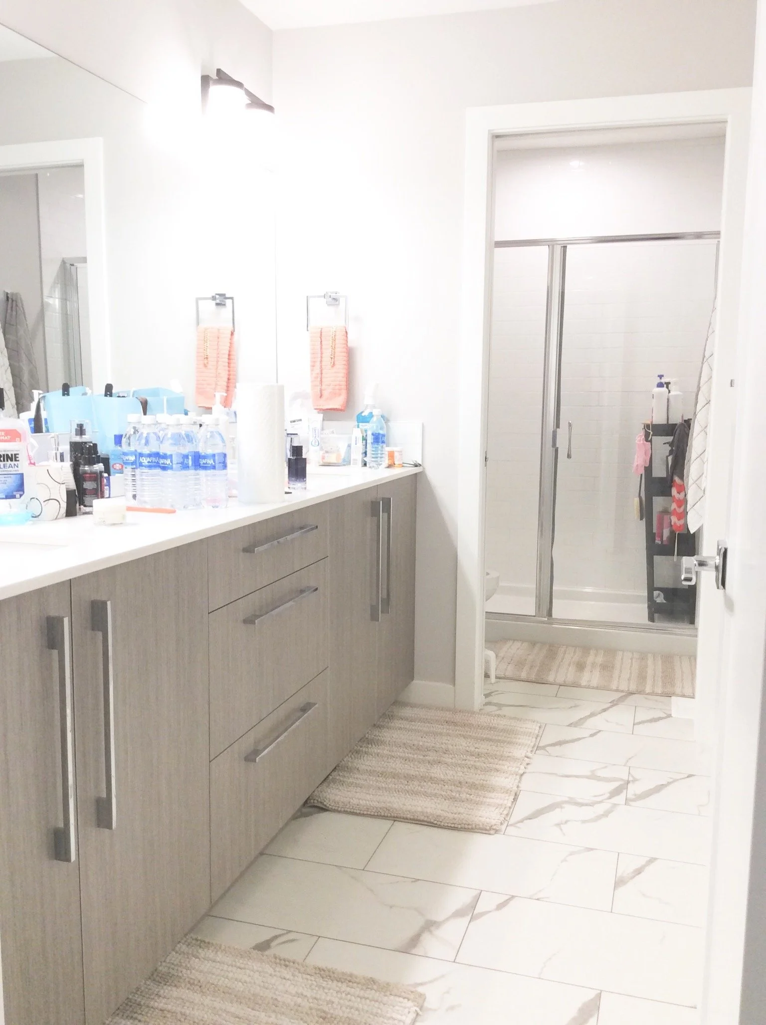 Modern bathroom with gray vanity, marble floor, towels, and shower with sliding door.