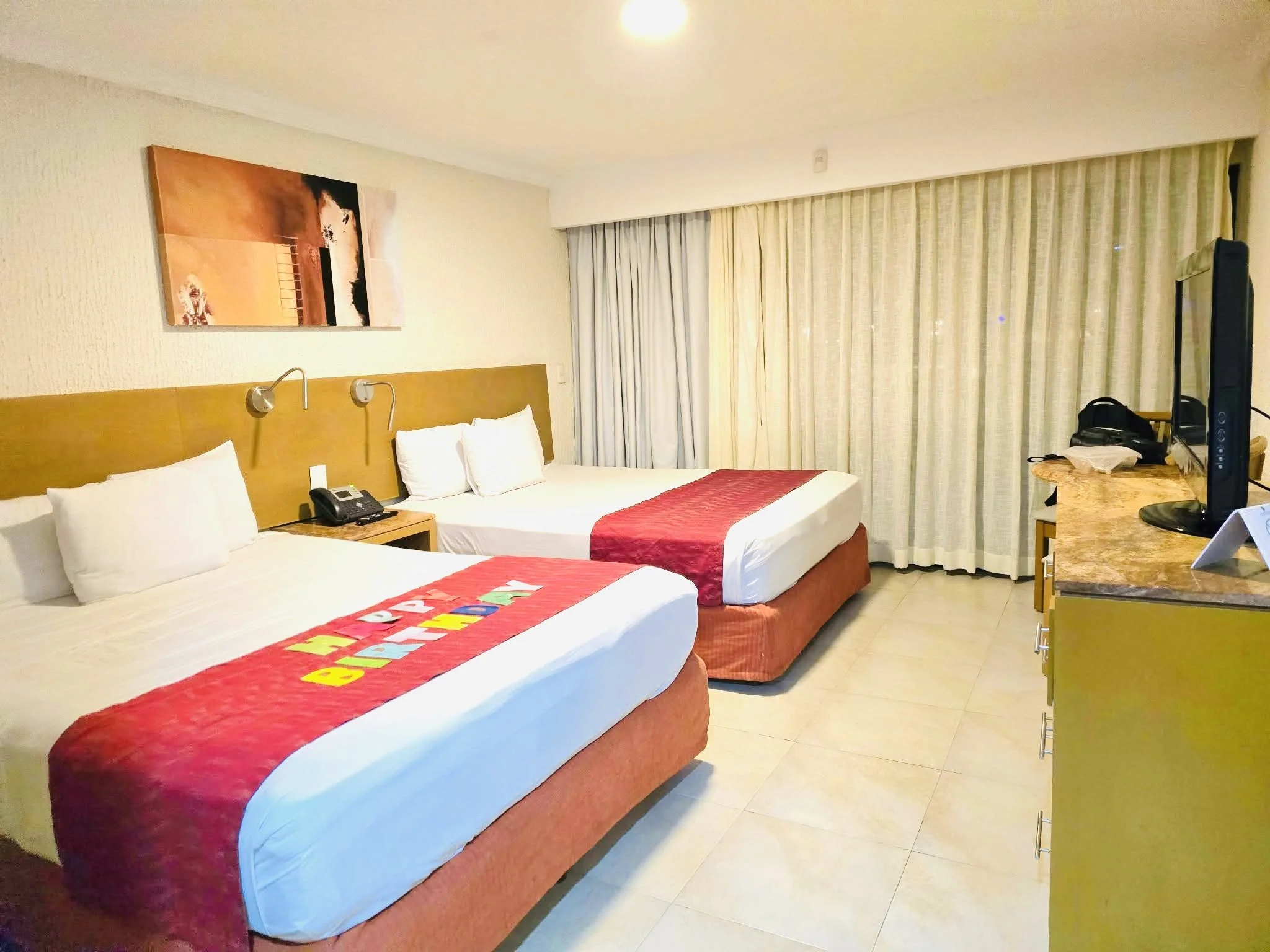 Hotel room with two beds, a desk with a TV, and a window with curtains.
