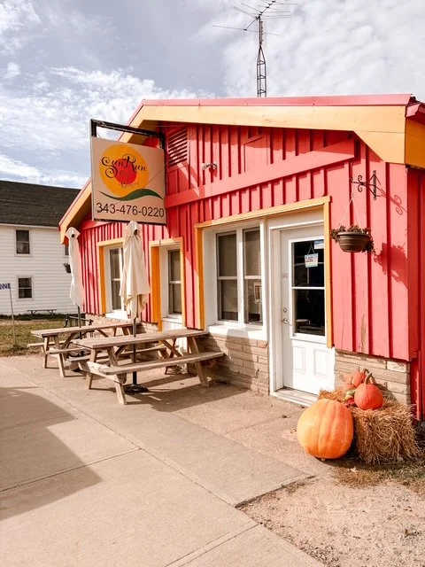 Exterior of a colorful red and yellow restaurant with outdoor seating, pumpkins, and hay bales in front.