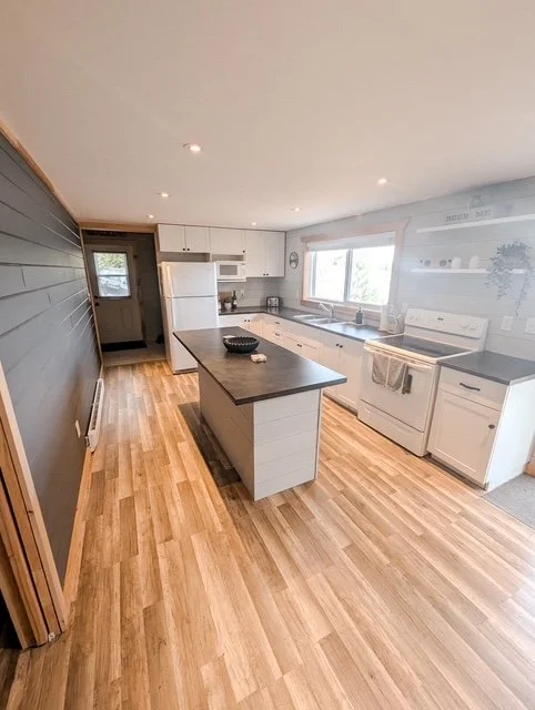 Kitchen with white cabinets, a center island, a window above the sink, and wood flooring.