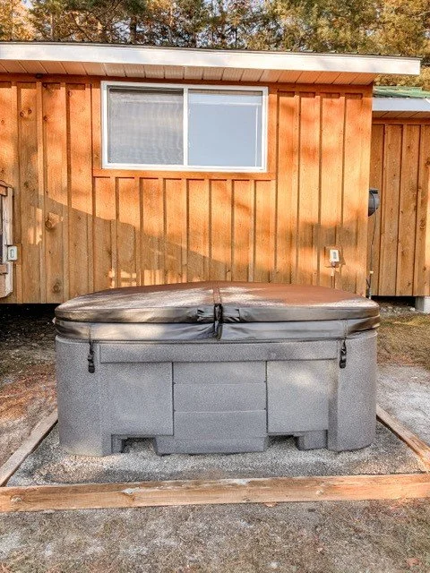 Hot tub with a cover in front of a wooden house with a window.