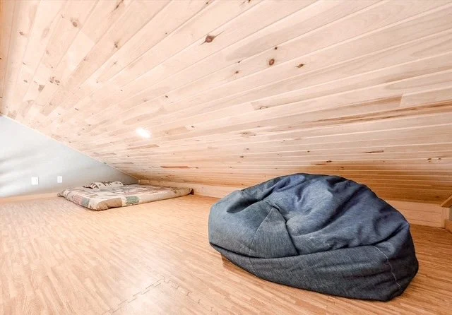 A cozy space with a sloped wooden-paneled ceiling, a small pillow on the floor, and a gray bean bag chair.
