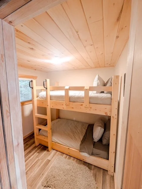 Wooden bunk bed in a small, cozy room with wood-paneled ceiling and a small window.