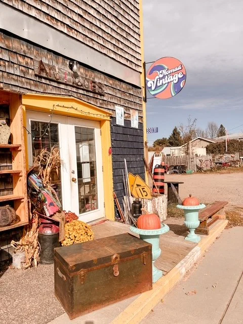 Exterior of a vintage shop called Nomad Vintage with a yellow and black building, pumpkins, and decorative items outside.