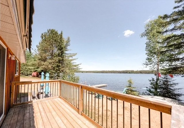 A wooden deck overlooking a large body of water with trees surrounding it, under a partly cloudy sky.