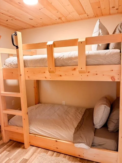 Wooden bunk bed with striped bedding and pillows in a cozy room with wood ceiling.
