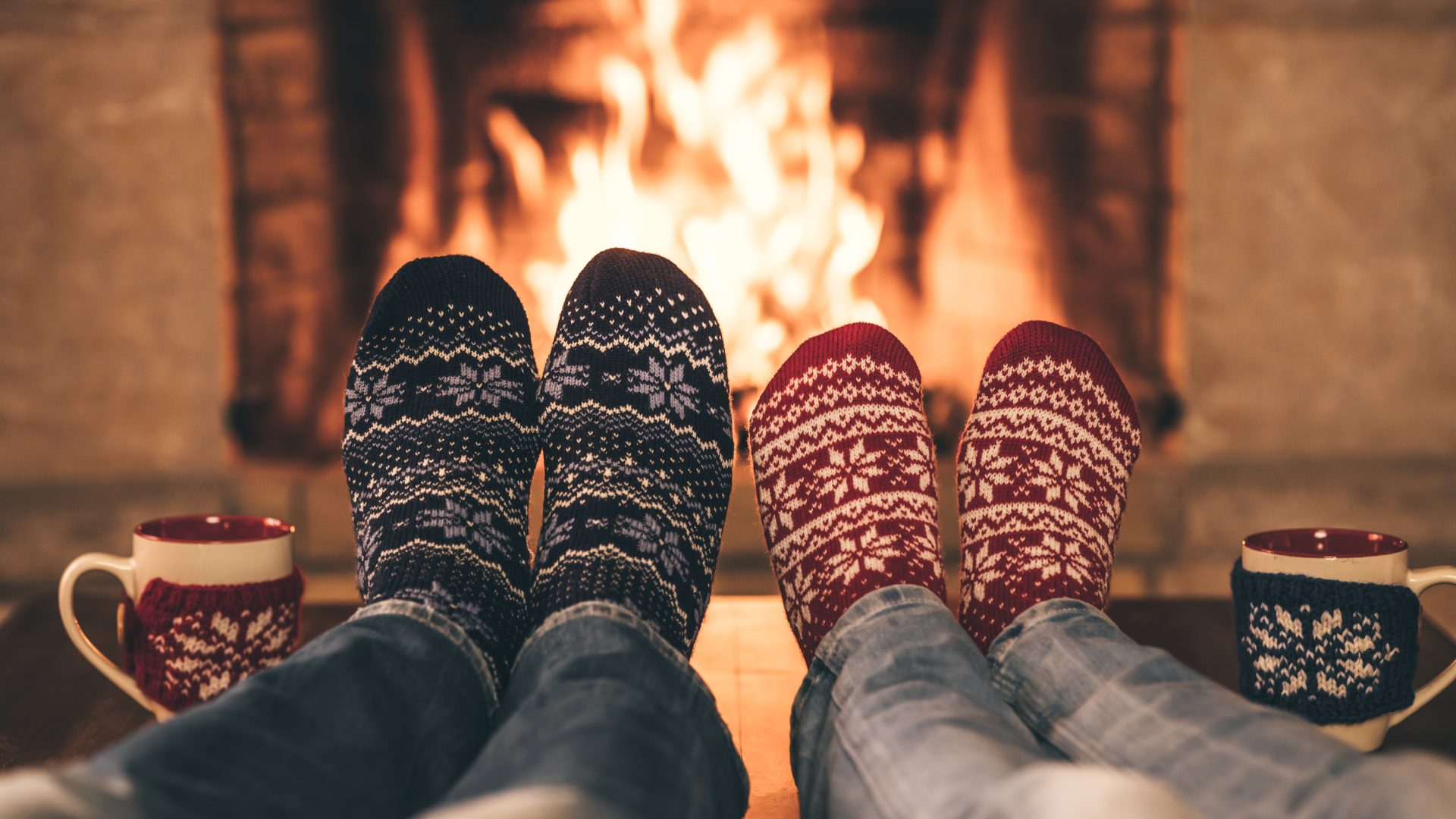 Two people's feet in warm cozy socks in front of a fireplace. Family Holidays