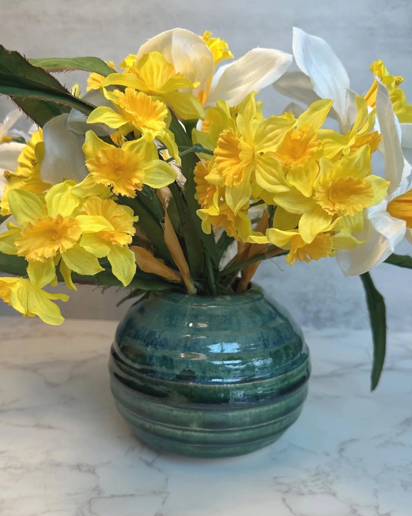 Handmade ceramic vase in ocean blue striated glaze holding yellow daffodils
