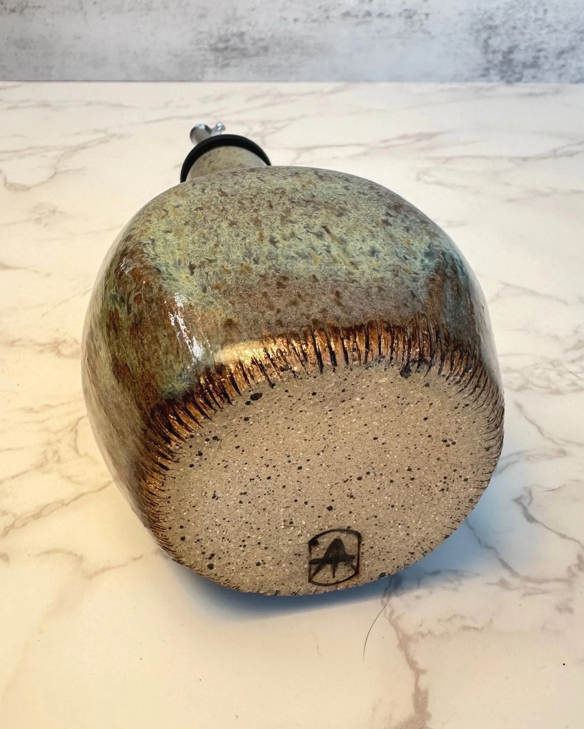 Bottom view of handmade ceramic oil dispenser with stainless steel pour spout in earthy green tones and speckled clay