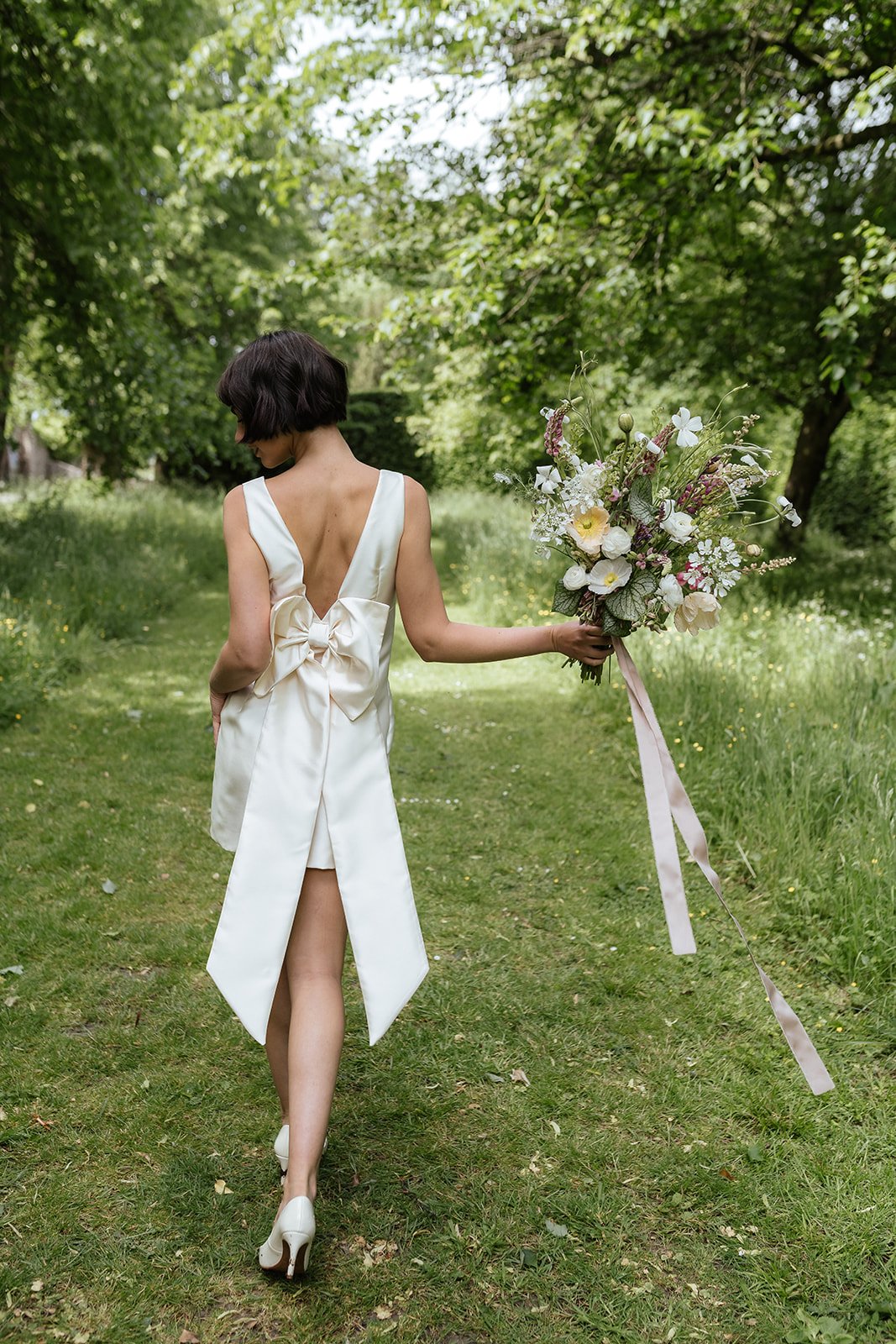 Woman in a white dress holding a large bouquet of flowers in a green outdoor setting.