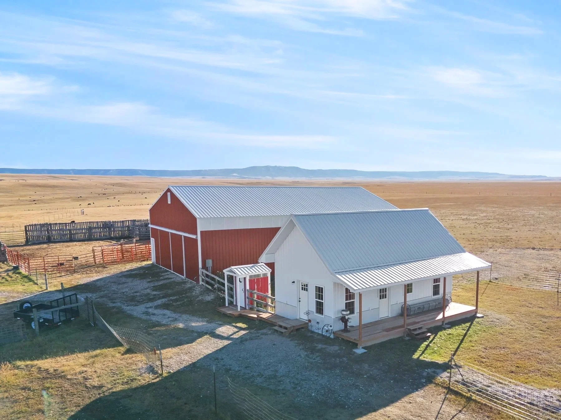 A white bunkhouse sits in front of a small red outhouse and big red barn