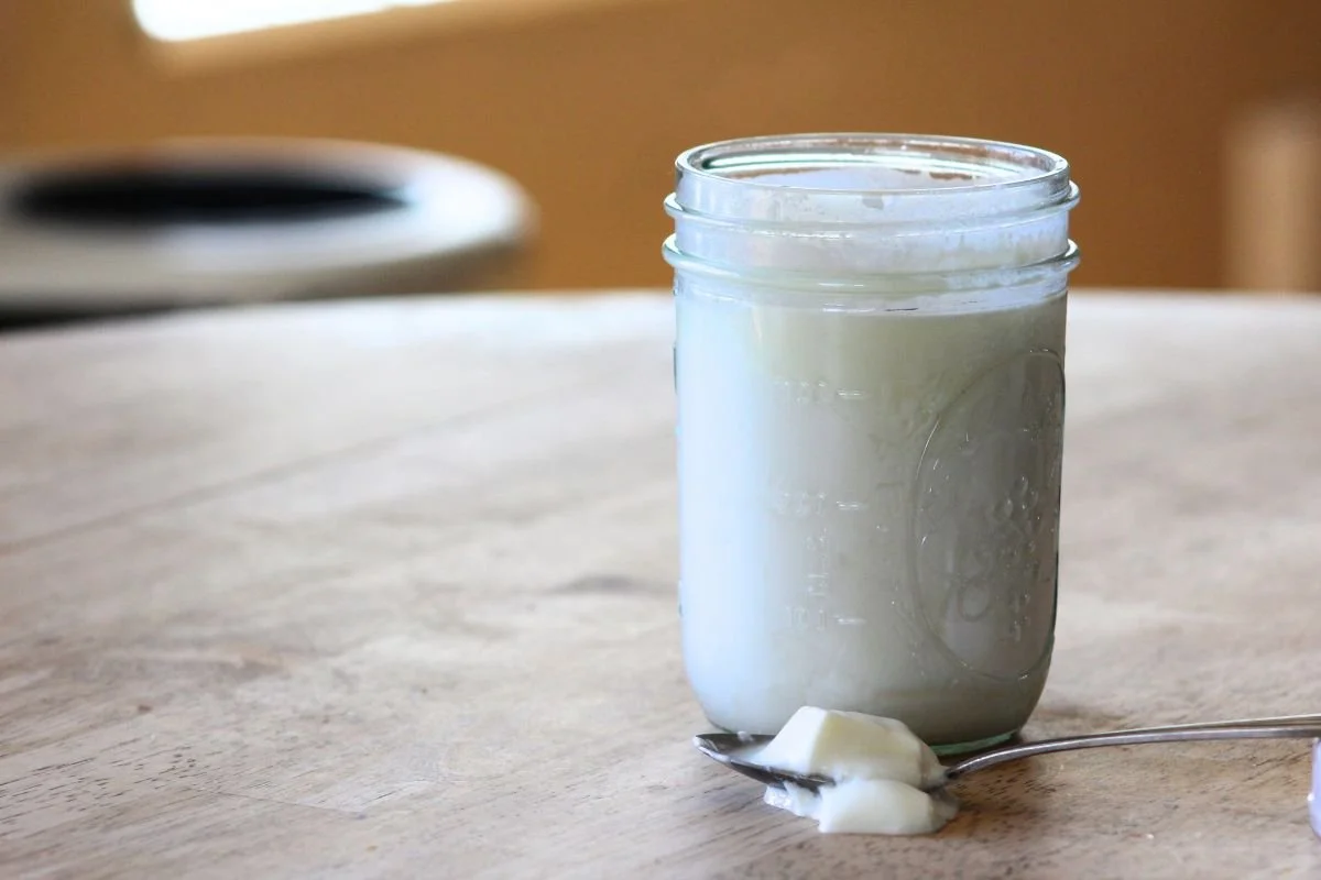 a jar of sheep milk clabber sits on a table with a spoonful of clabber sitting in front of the jar