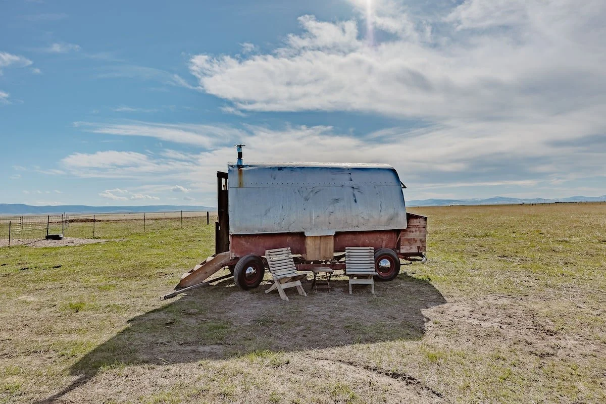 A sheepwagon sits out in front of a big blue sky