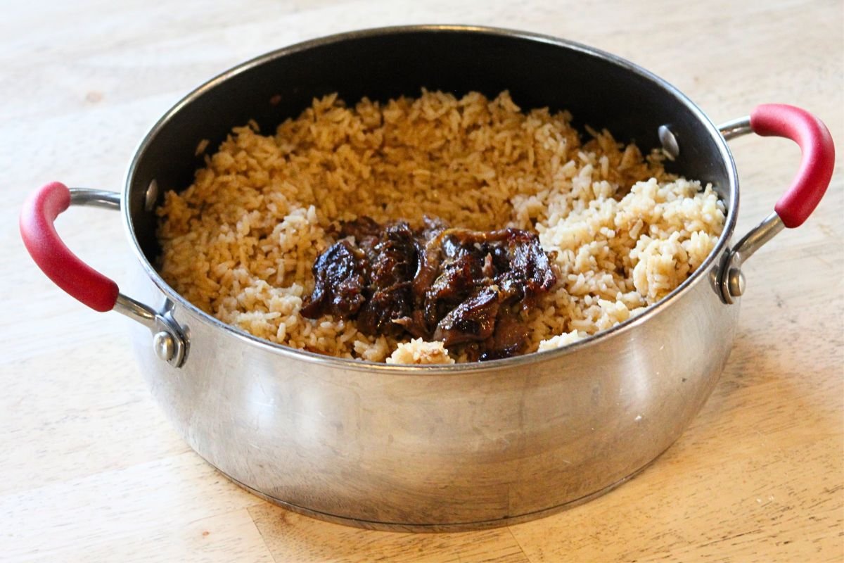 Roast lamb on top of garlic butter rice in a pot with red handles