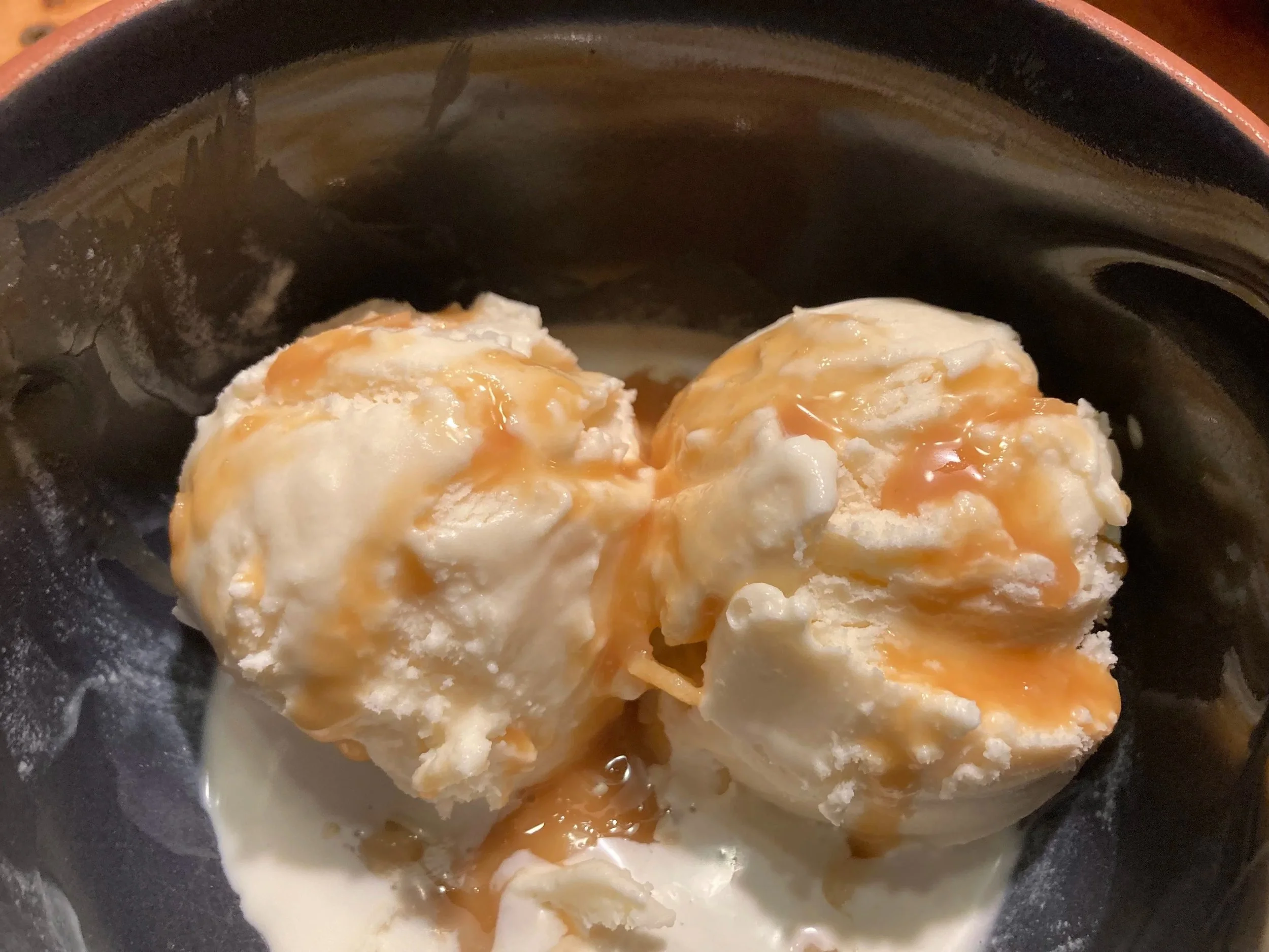 two scoops of vanilla ice cream are drizzled with caramel in a blue bowl