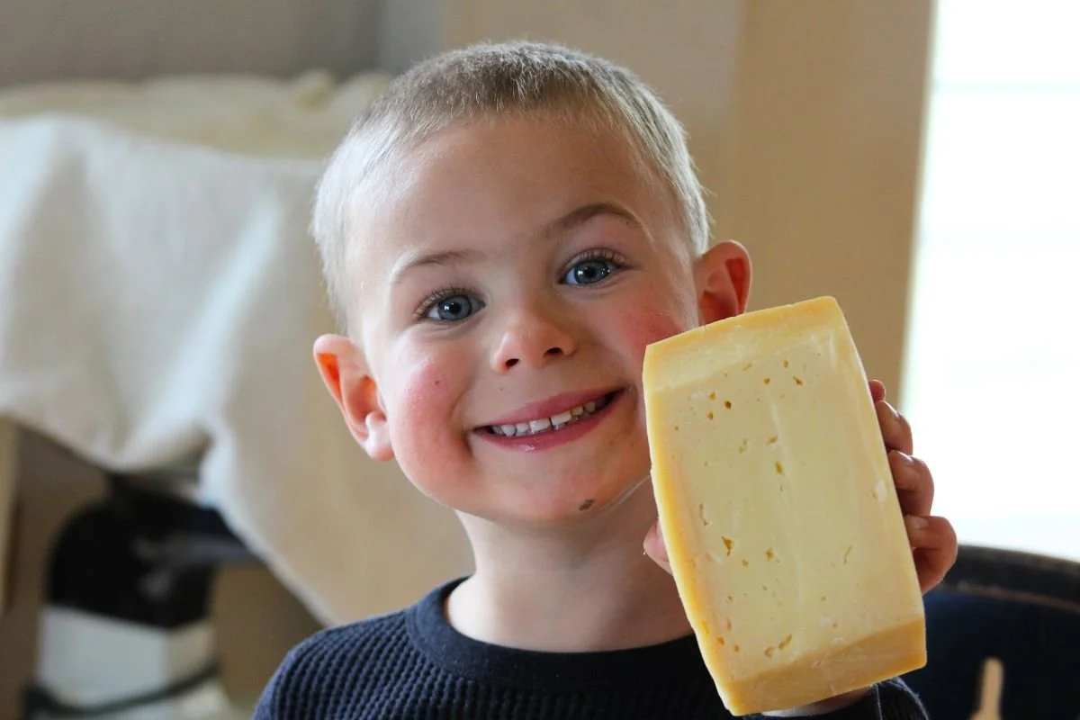 young smiling boy holding up a block of parmesan style cheese