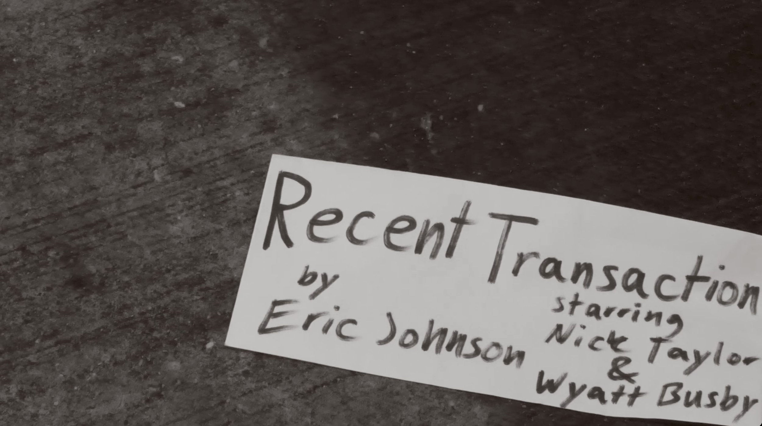 Close-up of a handwritten paper with the title 'Recent Transfer' and names of people on a dark surface.