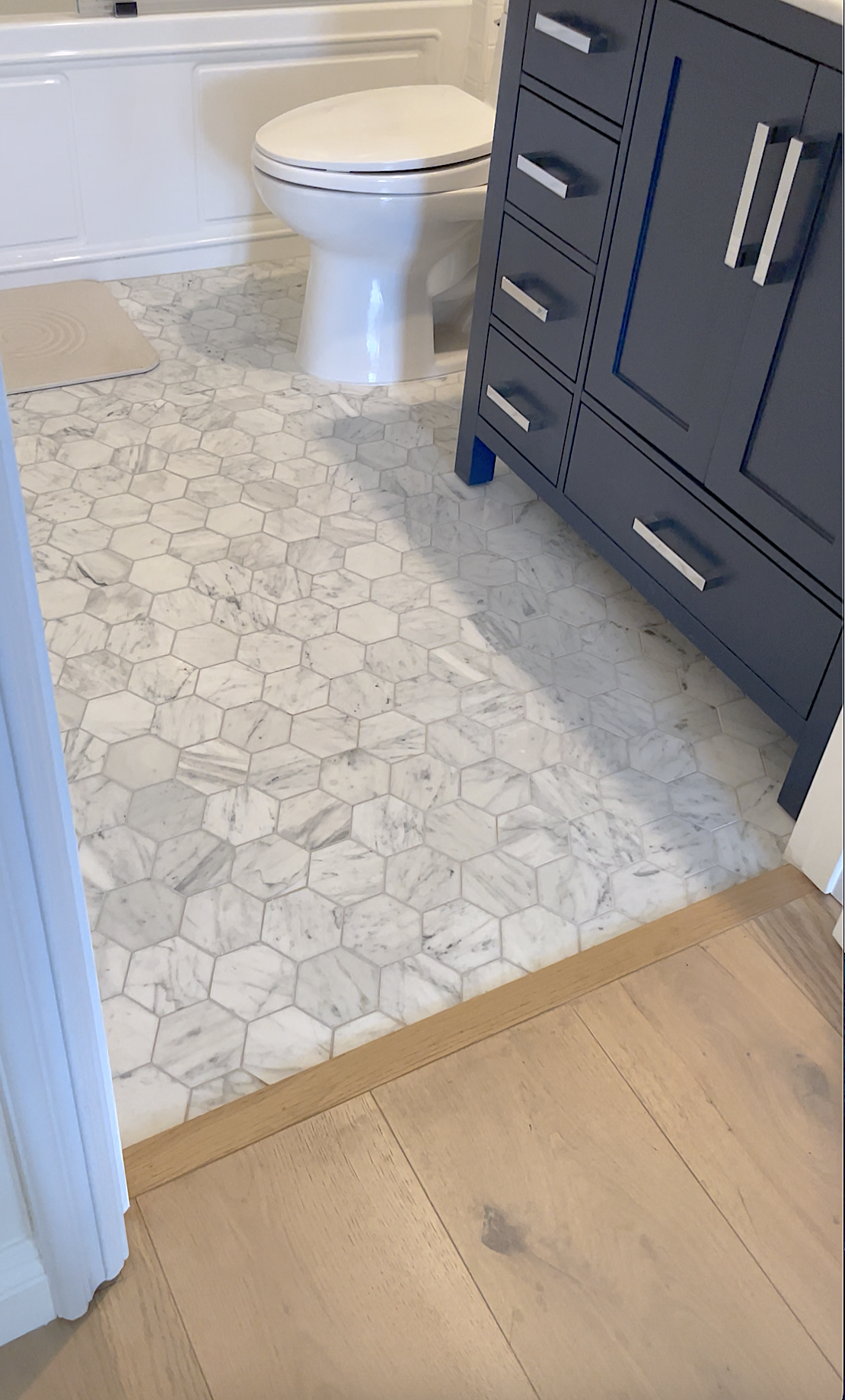 Bathroom with white hexagonal marble tile floor, a white toilet, and a blue vanity with silver hardware.