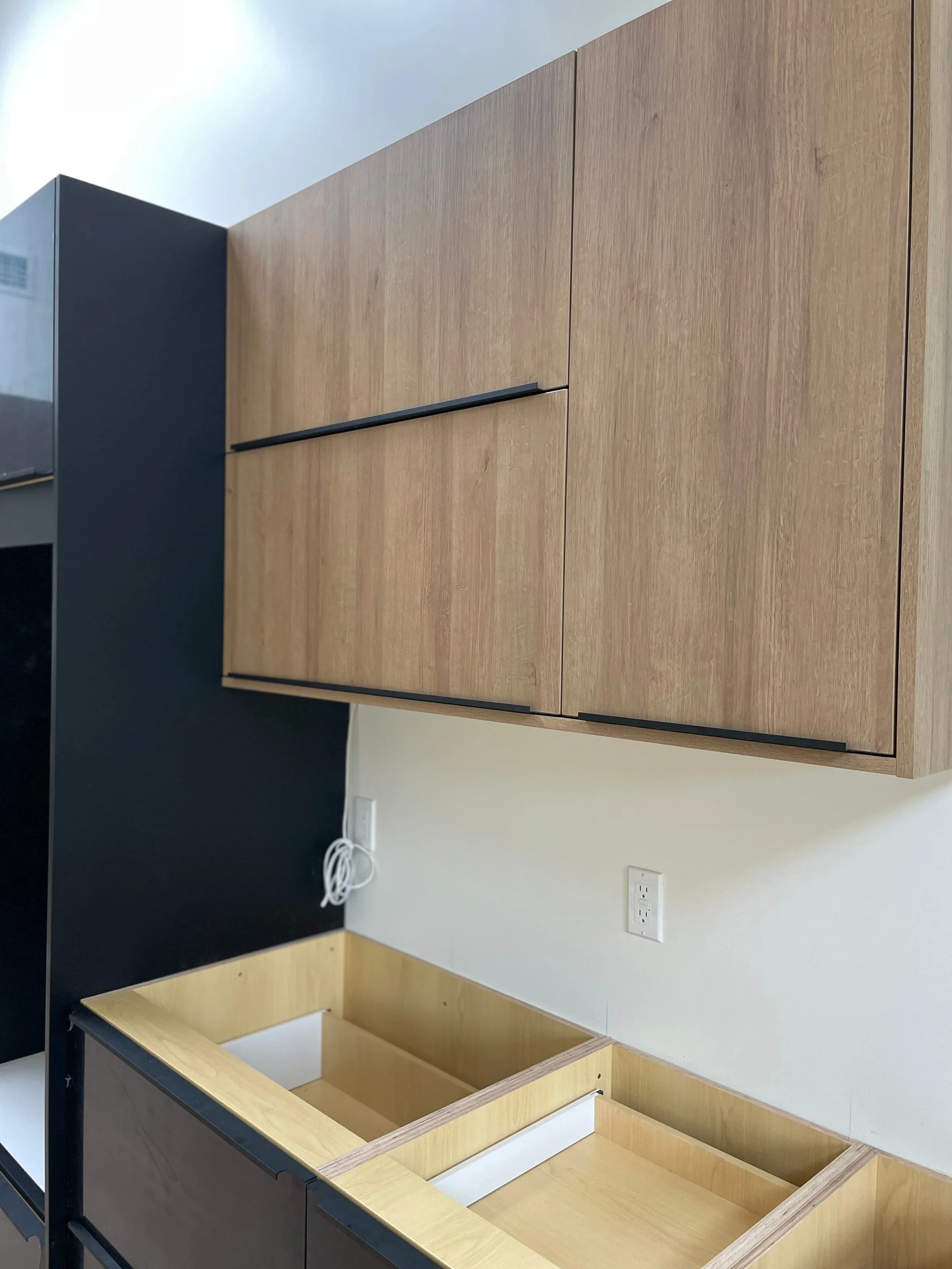 Modern house exterior with a black front door, second-story balcony with potted flowers, and exterior lighting at dusk.