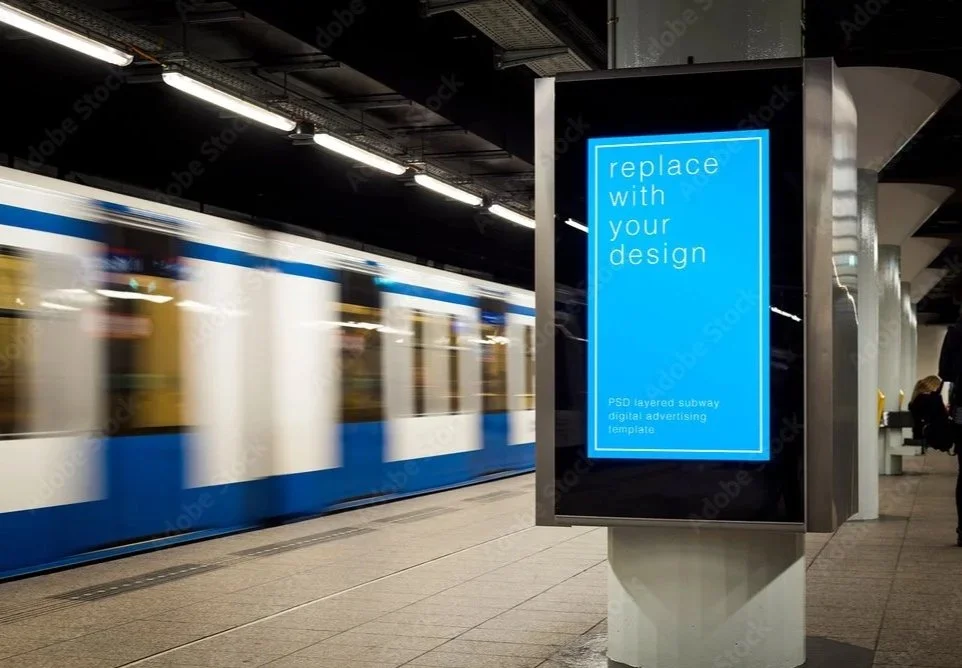 Digital advertising display in a subway station, showing placeholder text 'replace with your design' on a blue background.