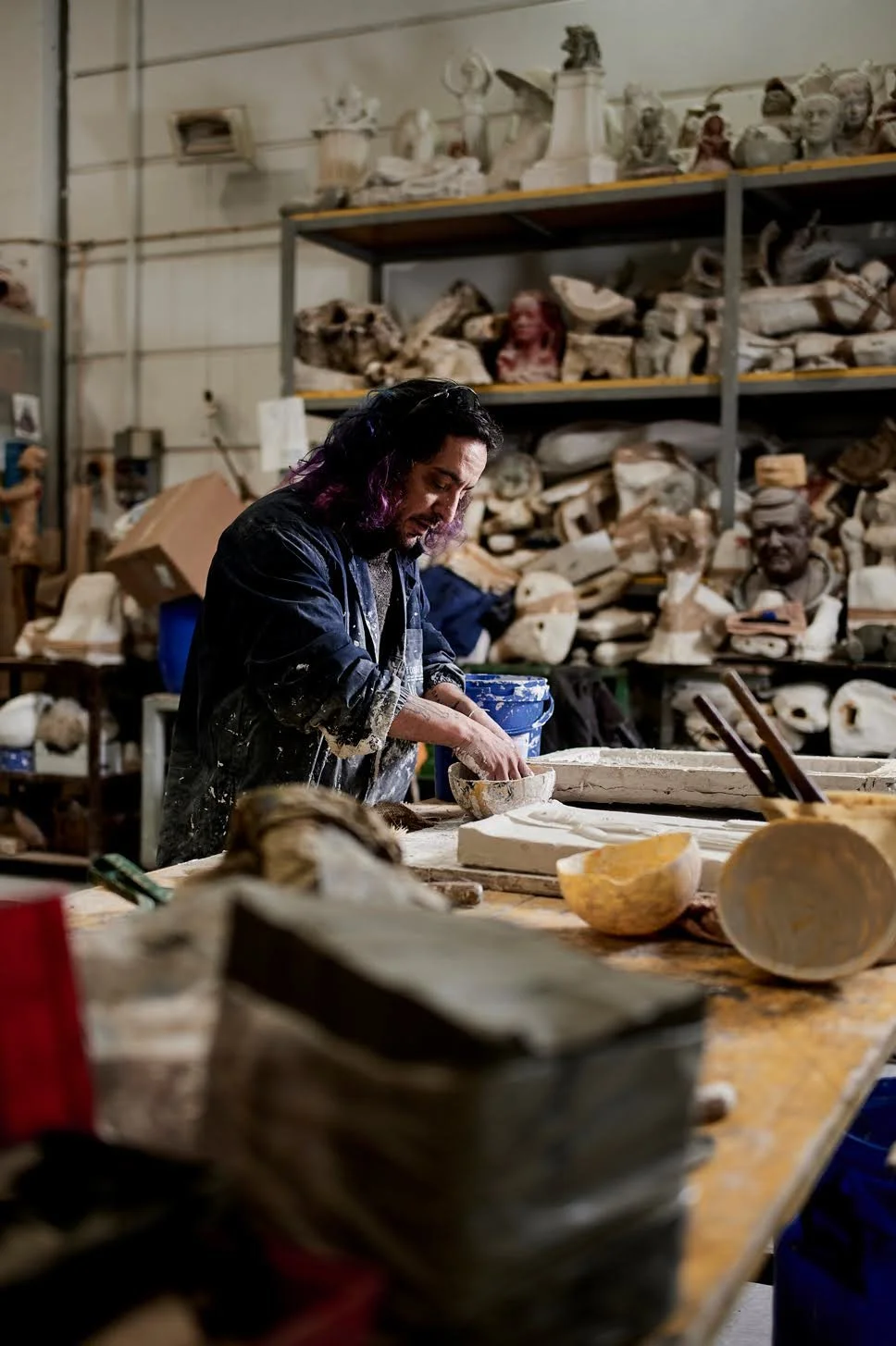 Leo Light Biaggi working at a sculpture workbench surrounded by tools and materials in his Florence, Italy studio.