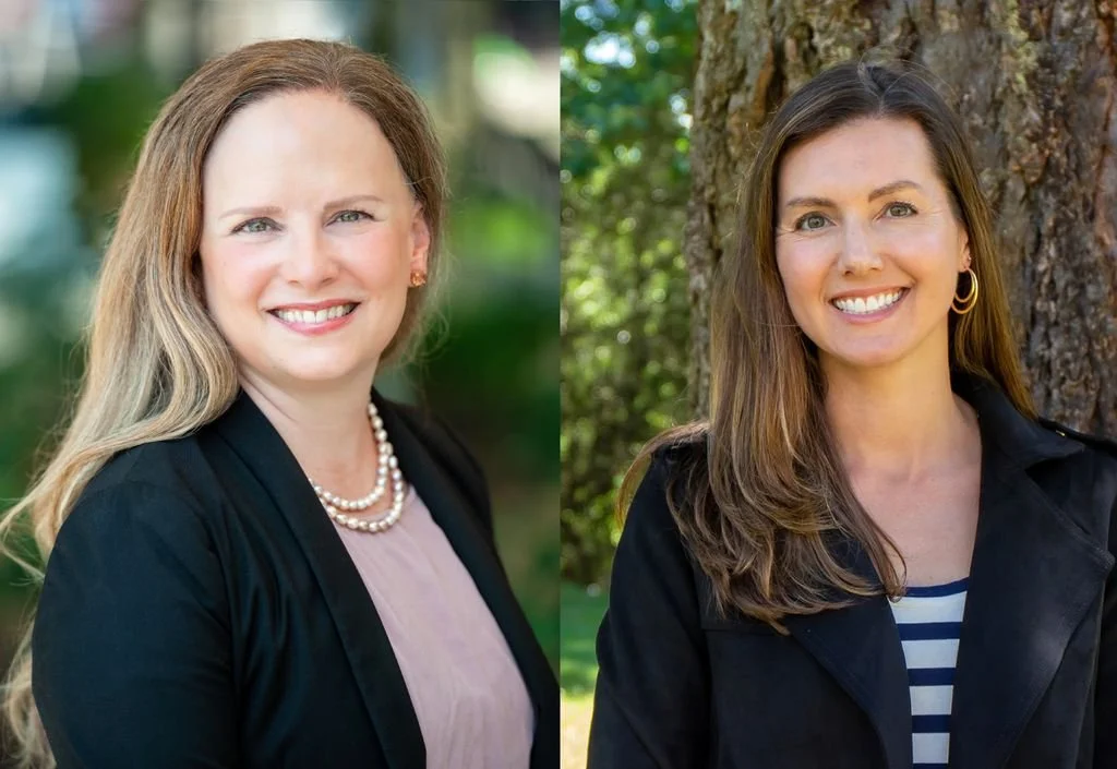 Person wearing a beige, fluffy sweater with one hand placed on their chest, sitting at a wooden table indoors.