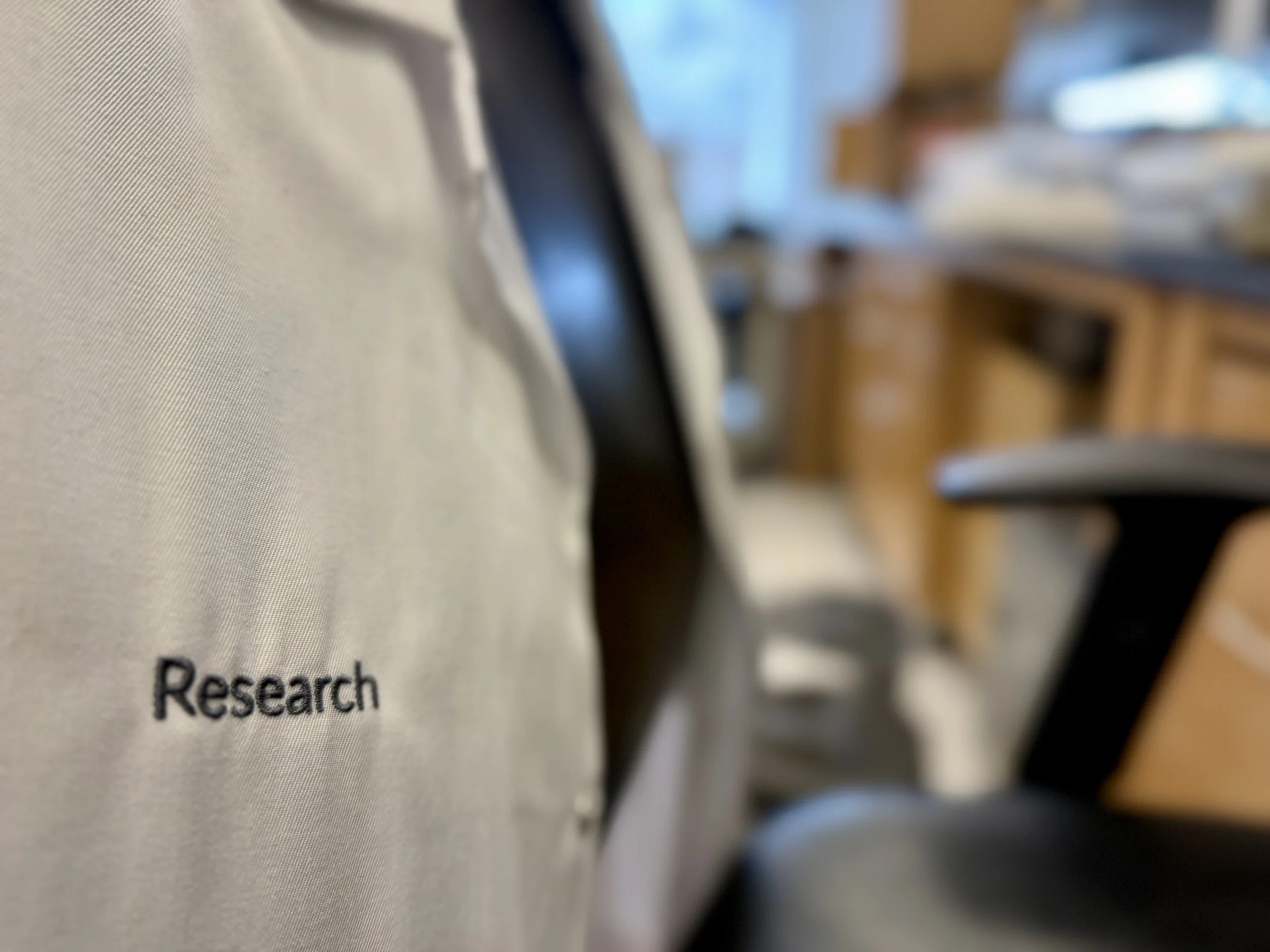 Close-up of a conference chair with the word 'Research' embroidered on its fabric, with a blurred background of a meeting room.