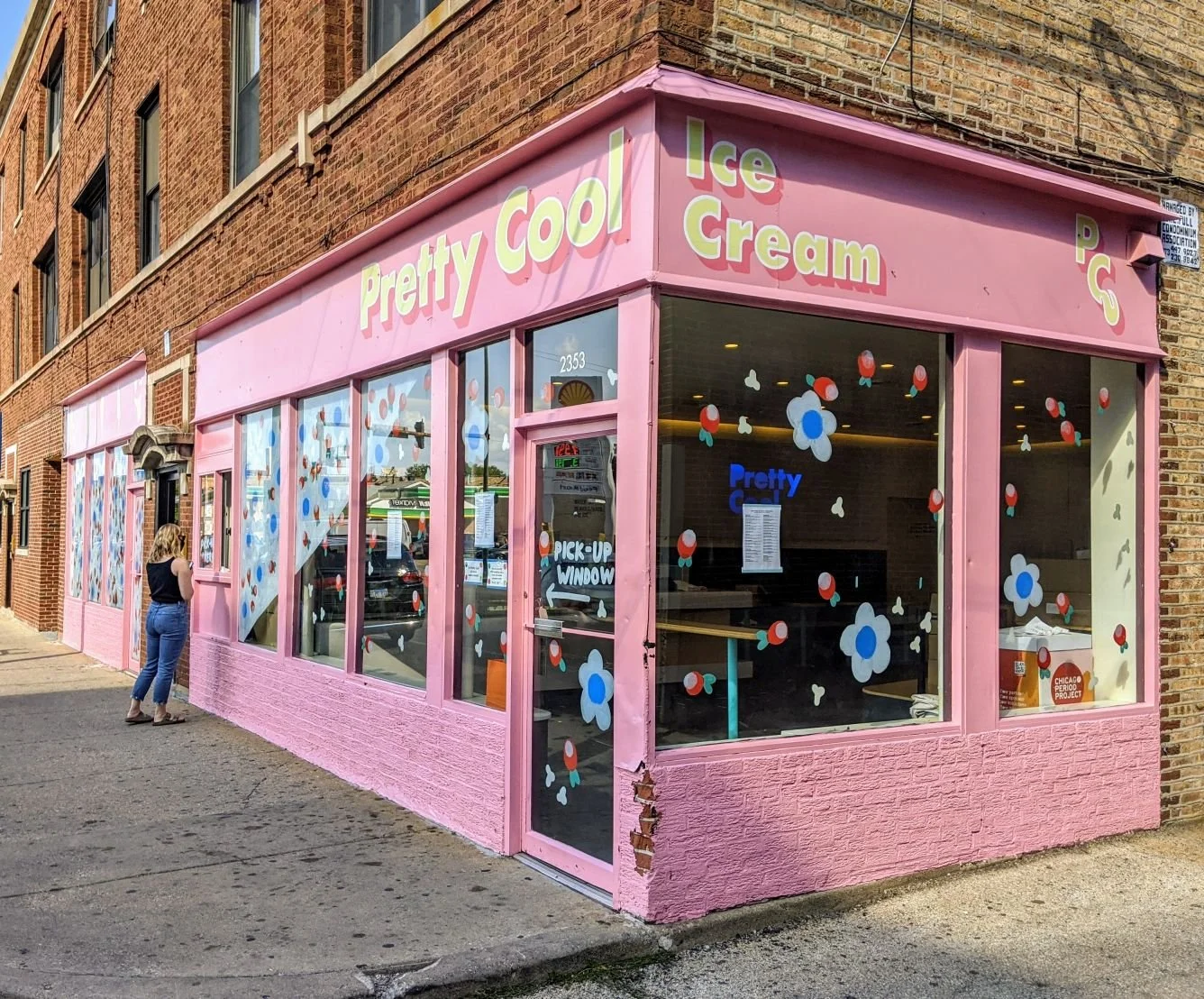 Person holding a colorful ice cream bar with rainbow sprinkles in front of a pink storefront.