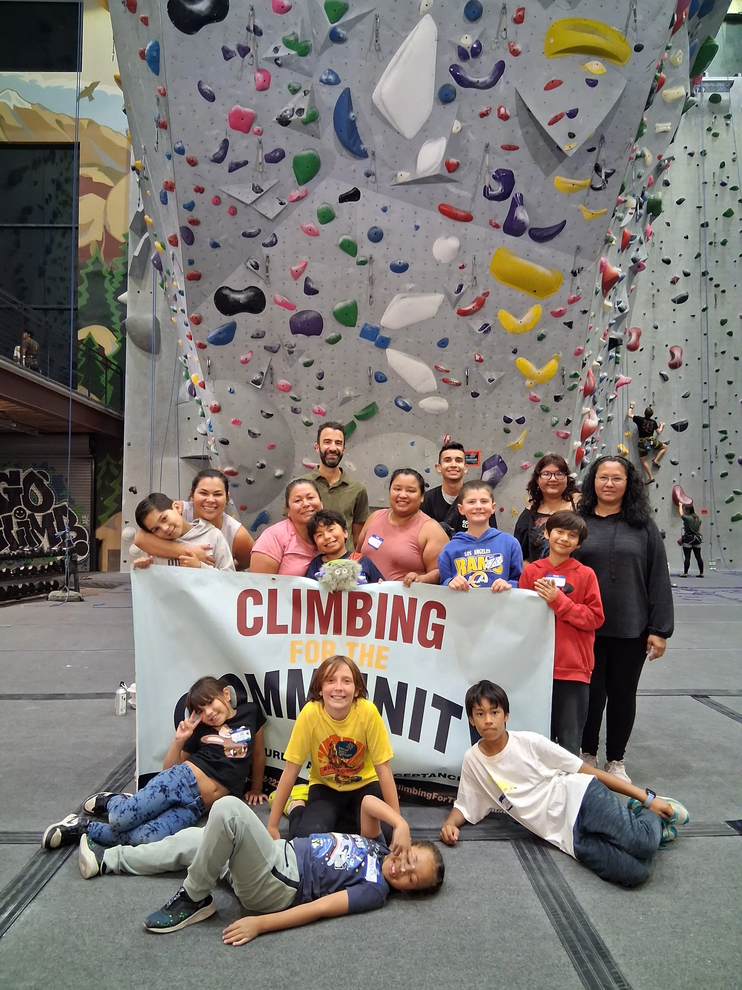 Children and adults in front of an indoor climbing wall holding a banner that reads