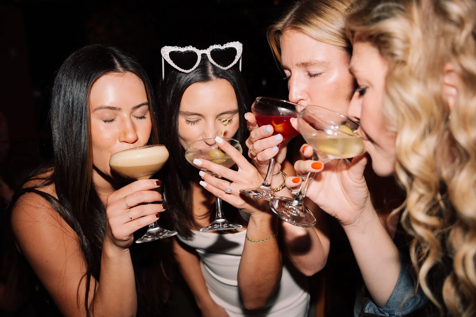 Group of four women drinking cocktails at a party.