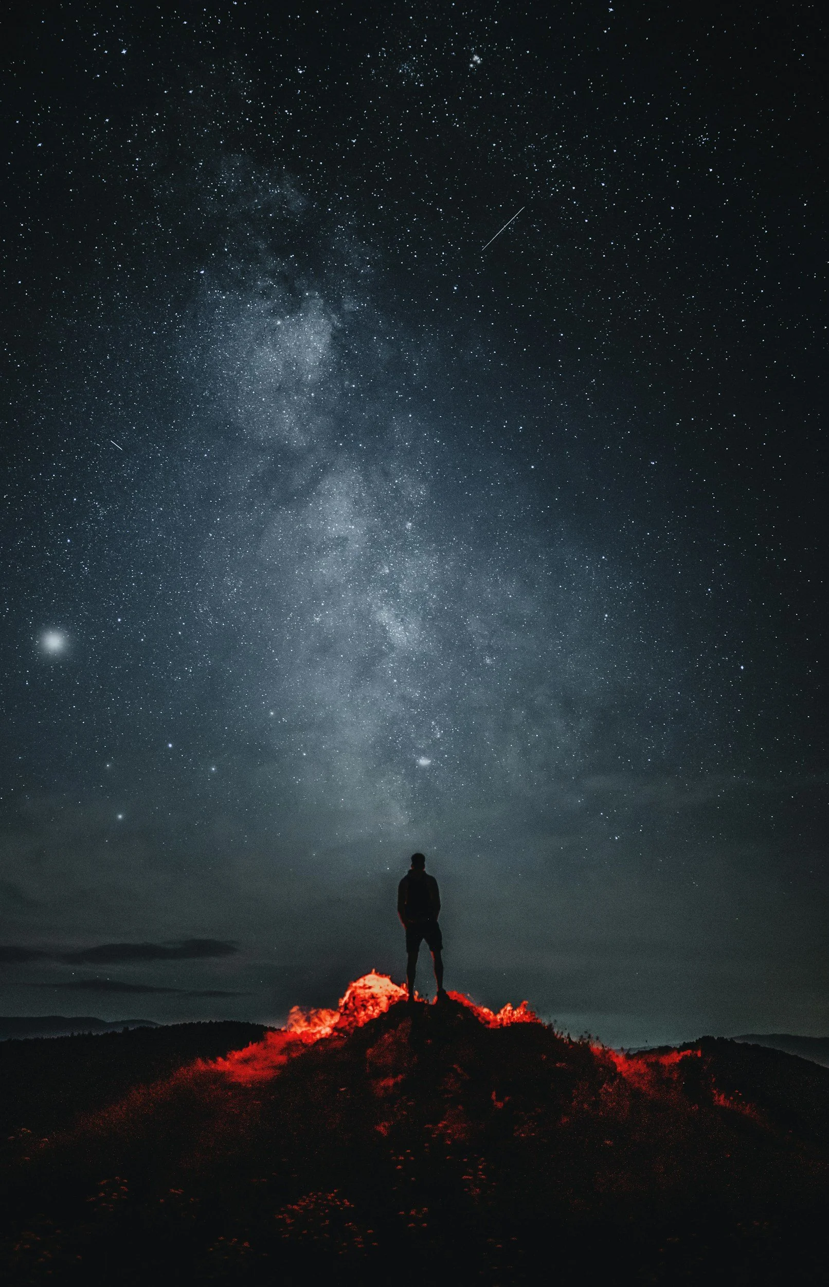 Silhouette of a person standing on a hill at night, looking up at a star-filled sky with the Milky Way galaxy visible.