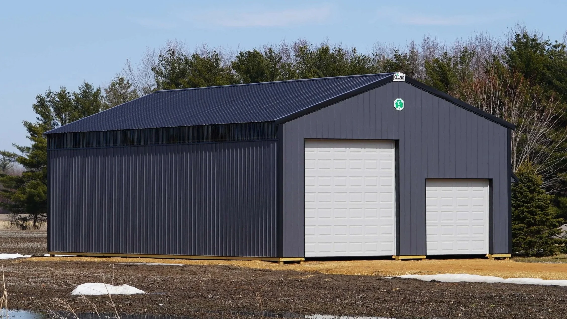 Dark gray metal building with two white roll-up doors set in a rural field.