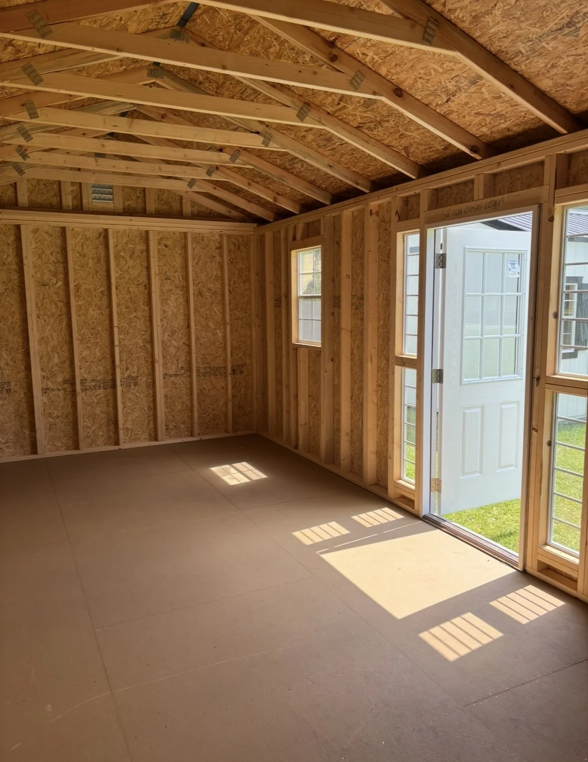 Interior of an unfinished shed featuring wood framing, multiple windows, and a full-glass door letting in natural light.