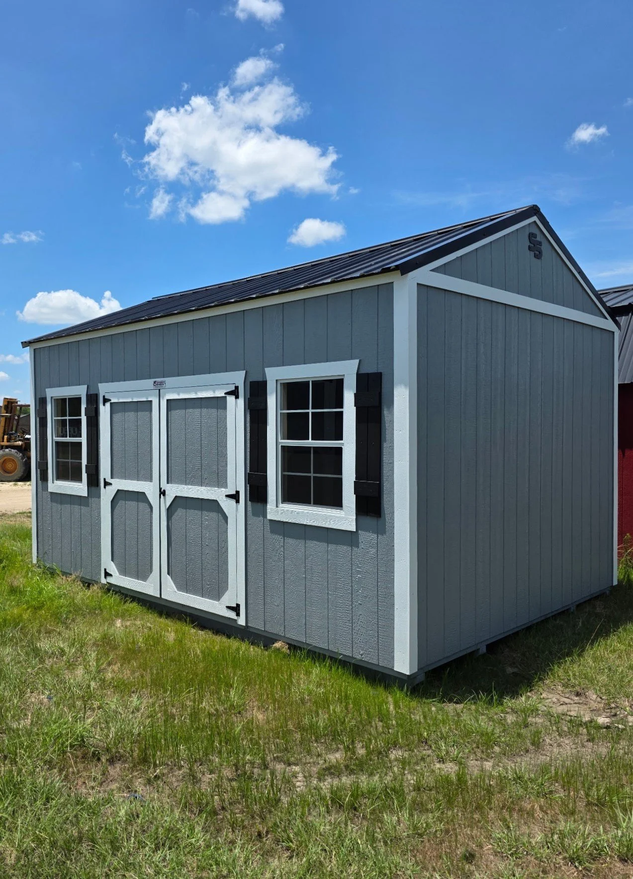 Gray painted shed with white trim, double front doors, and decorative shutters on the windows, set in a sunny outdoor lot.
