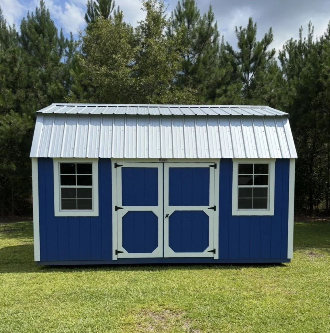 Blue barn-style shed with white trim and double front doors, situated on a grassy lawn with trees in the background.