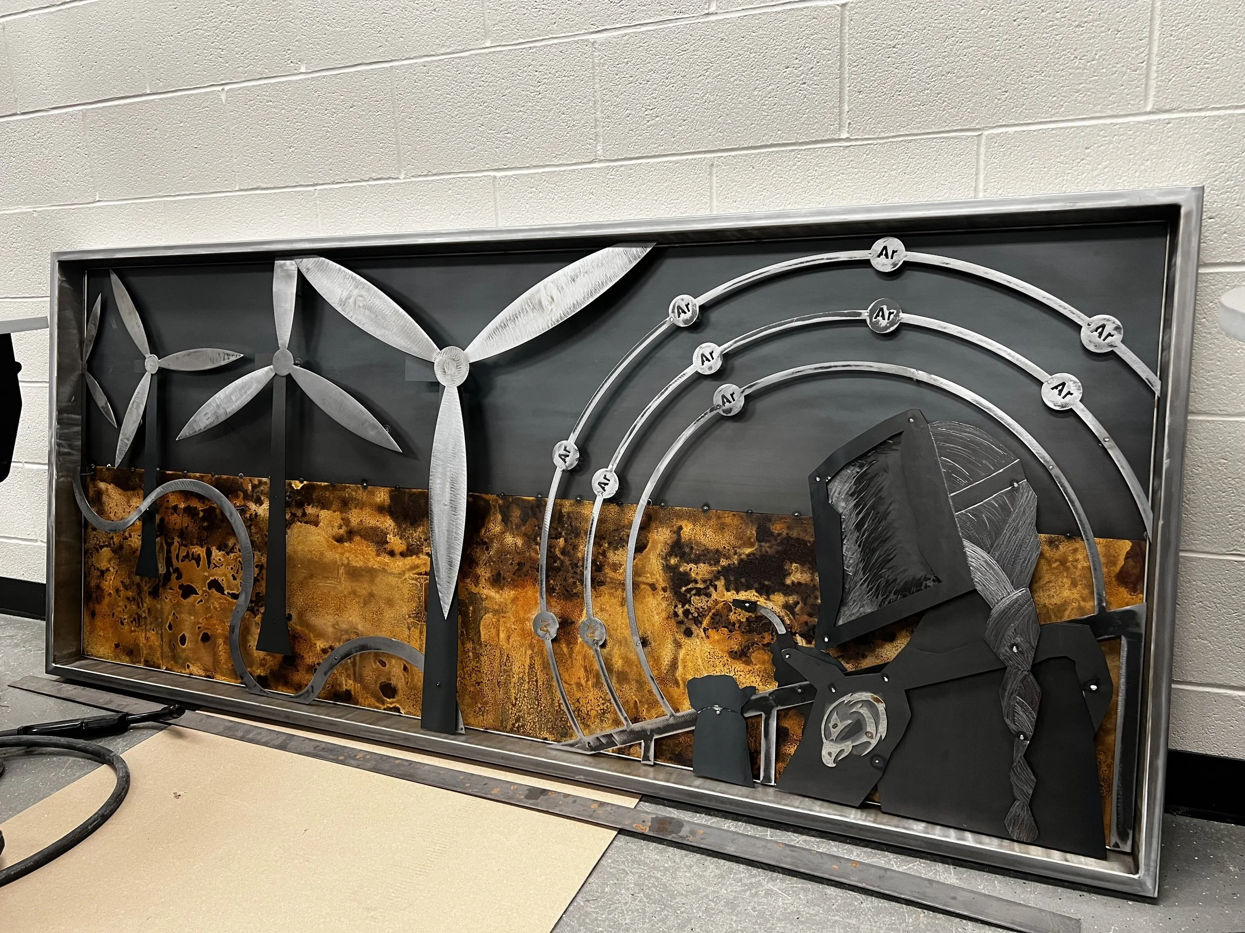 Large metal wall art installation with windmills and a welder, designed by Leif Armstrong and collaborators at Fanshawe College