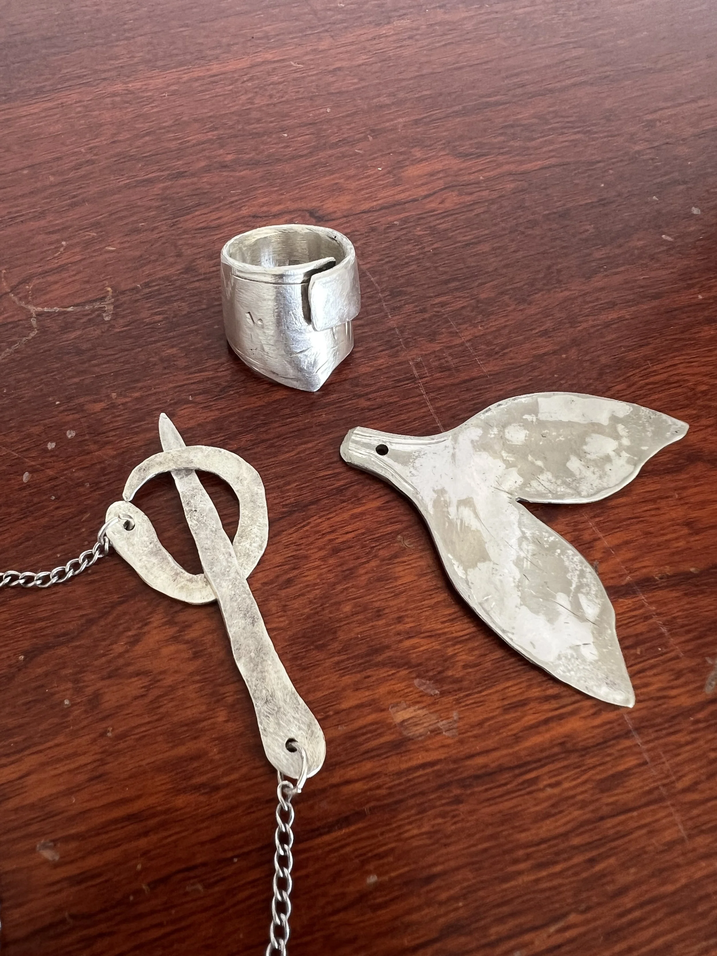 Custom silver jewellery set by Leif Armstrong including a forged ring, whale tail pendant, and sword-shaped necklace