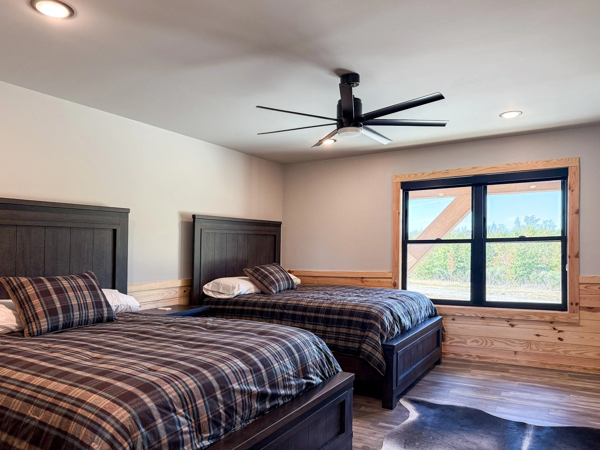 A bedroom with a dark wood bed frame and plaid bedding, a matching plaid pillow, a beige blanket, light-colored concrete floor, and wood-paneled walls