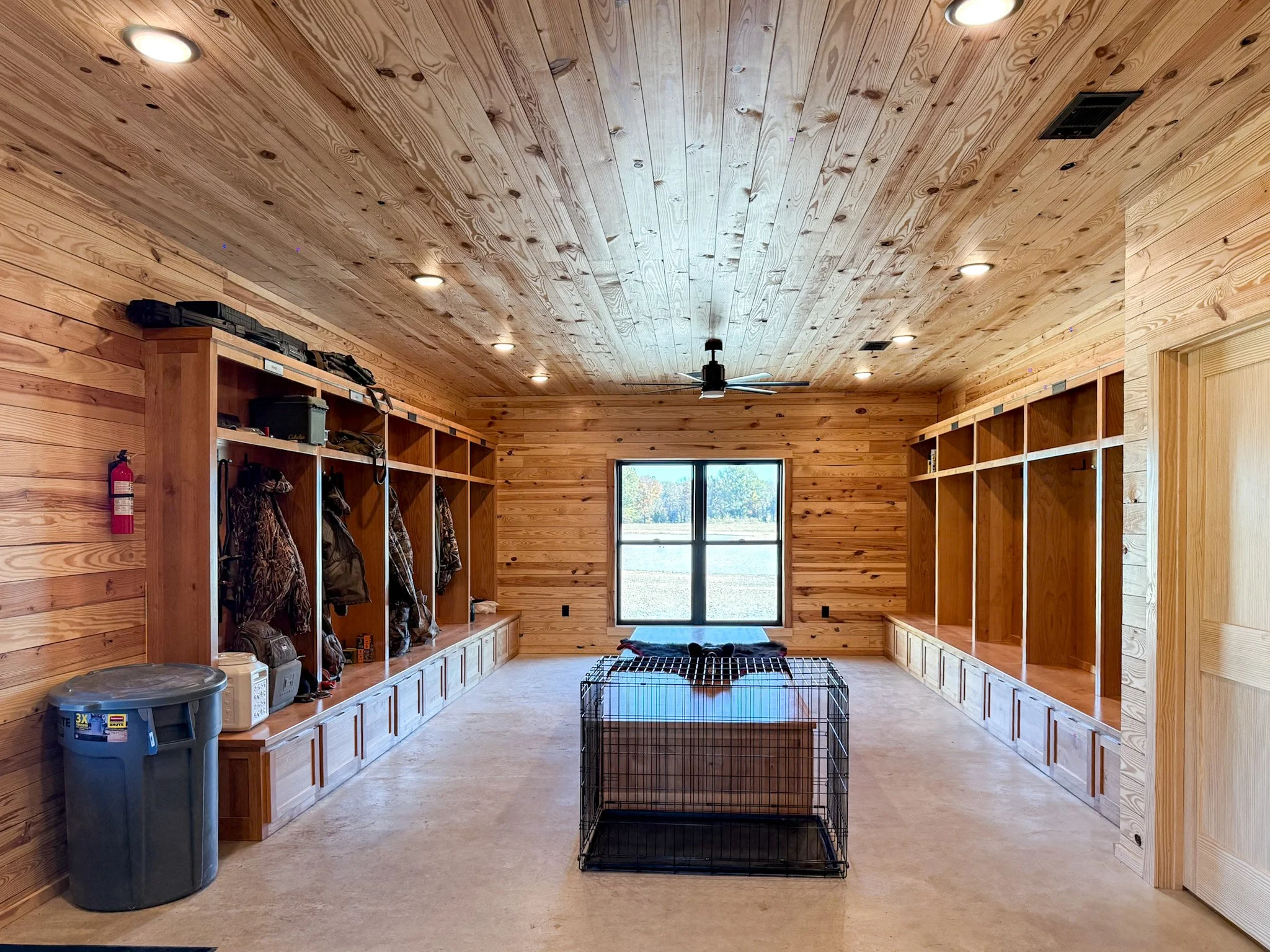 A wooden wall with hooks and shelves, a wooden door in the center, a coat hanging on the right, a patterned jacket on the left, a golf club and scarf hanging on the left, and a black and beige bag on the floor on the left.