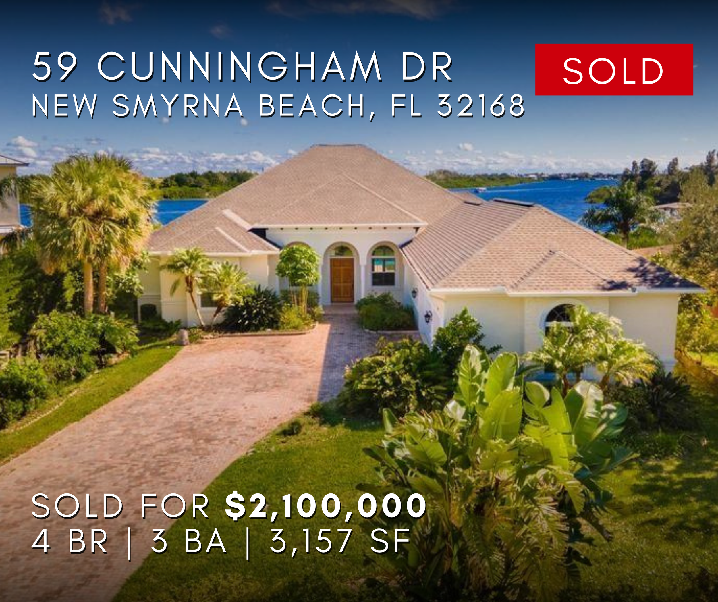 59 Cunningham Drive, New Smyrna Beach, Florida, with a brick driveway, lush green landscaping, palm trees, and a waterfront in the background. House Waterfront home Beach life. NSB Sold Home
